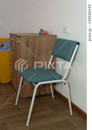 Minimalist teal folding chair positioned near a wooden dresser in a bright modern room. 140680449