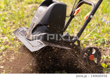 Powerful electric garden tiller machine cultivating dark soil in a bright green sunny field. Powerful electric garden tiller machine cultivating dark soil in a bright green sunny field. 140680456