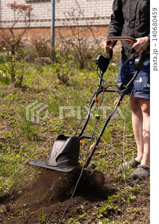 Man using electric garden tiller to cultivate soil in sunny backyard garden. 140680459