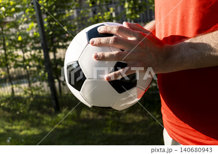 Man in a red T shirt holding a black and white soccer ball outdoors, echoing popular team kits and global world cup imagery. Man in a red T shirt holding a black and white soccer ball outdoors, echoing popular team kits and global world cup imagery. 140680943