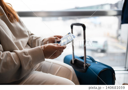 Passenger holding passport and tickets next to blue suitcase Passenger holding passport and tickets next to blue suitcase 140681039