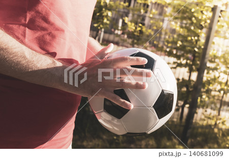 Person in a red T shirt holding a black and white soccer ball outdoors, reflecting a connection to the global soccer World cap. Person in a red T shirt holding a black and white soccer ball outdoors, reflecting a connection to the global soccer World cap. 140681099