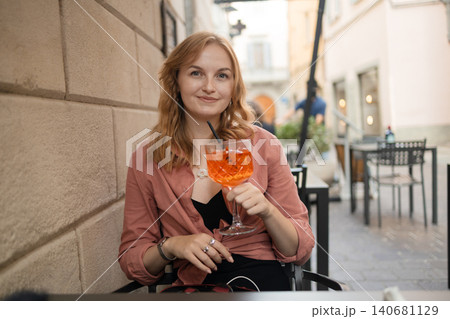 Beautiful young woman sitting at outdoor cafe with Aperol Spritz cocktail on summer vacation Beautiful young woman sitting at outdoor cafe with Aperol Spritz cocktail on summer vacation 140681129