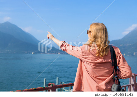 Young female tourist pointing at beautiful mountain lake view during summer vacation 140681142