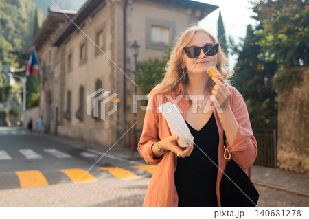 Young blonde woman eating traditional cookie on a city street Young blonde woman eating traditional cookie on a city street 140681278