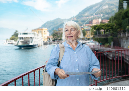 Happy senior woman tourist with a map at Lake Como Happy senior woman tourist with a map at Lake Como 140681312
