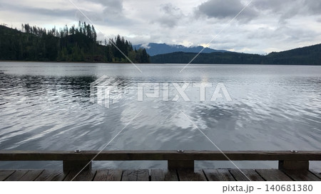 Wooden dock overlooking a calm mountain lake reflection 140681380