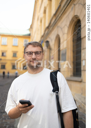 Smiling young man with glasses holding smartphone in city Smiling young man with glasses holding smartphone in city 140681401