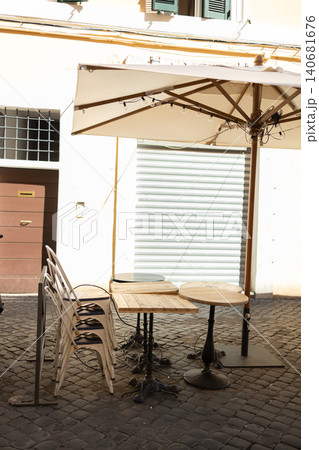 Closed outdoor street cafe terrace with folded umbrellas and empty tables on a sunny day. Closed outdoor street cafe terrace with folded umbrellas and empty tables on a sunny day. 140681676
