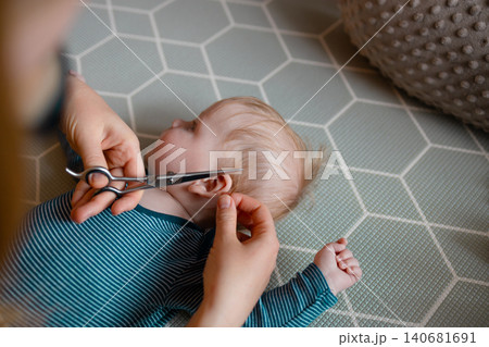 Close-up of a mother carefully trimming her baby son's hair with scissors 140681691