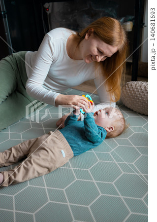 Happy mother playing with her infant baby boy on the floor at home Happy mother playing with her infant baby boy on the floor at home 140681693