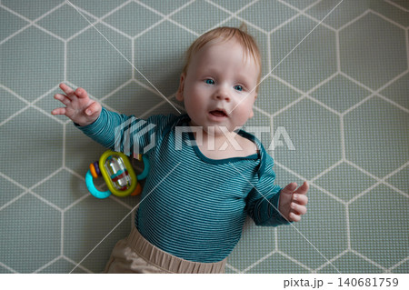 Adorable baby lying on soft play mat and playing with colorful toy, top view perspective, early development, curiosity and parenting concept. Adorable baby lying on soft play mat and playing with colorful toy, top view perspective, early development, curiosity and parenting concept. 140681759