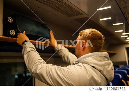 Man placing luggage on overhead shelf inside train Man placing luggage on overhead shelf inside train 140681763