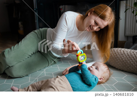 Happy mother playing with her infant baby boy on the floor at home Happy mother playing with her infant baby boy on the floor at home 140681810