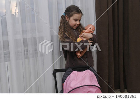 girl standing indoor near stroller holding baby doll, girl standing indoor near stroller holding baby doll, 140681863