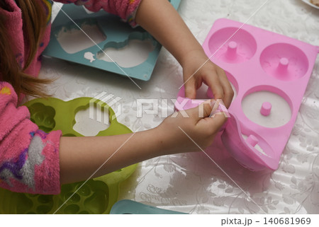 Kid takes hardened gypsum shapes out of silicone trays on crafting table. 140681969