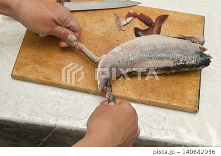 Professional cook cleaning salty herring on wooden board. Professional cook cleaning salty herring on wooden board. 140682036