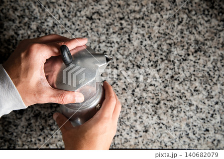 A person is holding a silver coffee pot with a lid on it A person is holding a silver coffee pot with a lid on it 140682079