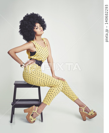 Black woman, portrait and retro in studio, vintage and hand on waist, unique and dots in clothes. Fashion, hippy and person with hair, model and strong African lady, yellow and girl sitting in chair 140682293