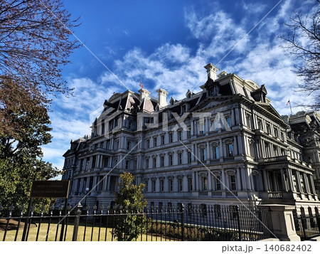 A side view of the Dwight D. Eisenhower Executive Office Building, empty of people, on a bright sunny day, framed by park trees. A side view of the Dwight D. Eisenhower Executive Office Building, empty of people, on a bright sunny day, framed by park trees. 140682402