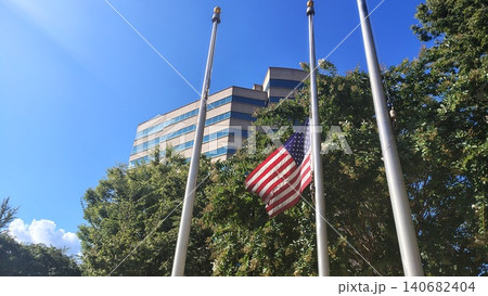 The U.S. national flag flutters against a multi-story building on a bright sunny day. The shot is taken from a low angle, looking upward. The flag is positioned approximately halfway up the mast. The U.S. national flag flutters against a multi-story building on a bright sunny day. The shot is taken from a low angle, looking upward. The flag is positioned approximately halfway up the mast. 140682404