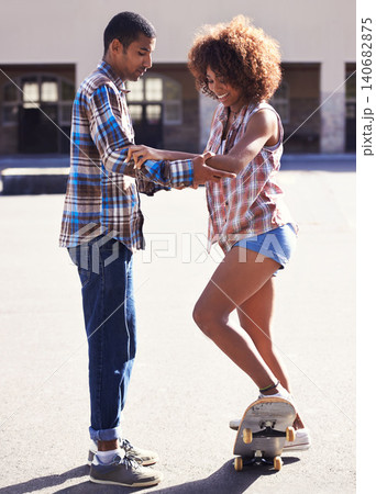 Happy, learning and man with woman on skateboard in city on romantic and fun date together. Smile, couple and African male skater teaching skating to young girlfriend in urban town with love. 140682875