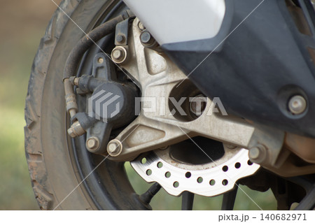 Motorcycle wheel brake disc caliper rotor tire suspension close up of front disc brake assembly, metal hub and bolts, outdoor background, rugged mechanical detail 140682971