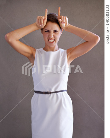 Woman, portrait and hand for horn in studio, silly face and playful body language on gray background. Female person, humor and funny expression for communication or emotion or symbol for mocking 140683133