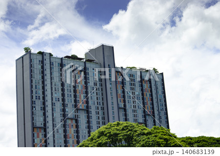High rise apartment building under cloudy sky with green tree foreground High rise apartment building under cloudy sky with green tree foreground 140683139