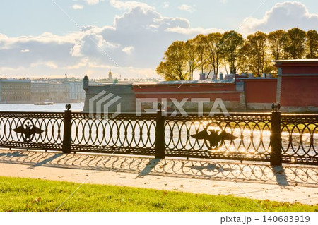 Isaac cathedral, Winter Palace, picturesque metal railings with a double-headed eagle and the crown of the Russian Empire on embankment in St. Petersburg, autumn sunset, incredible sun glare, Russia Isaac cathedral, Winter Palace, picturesque metal railings with a double-headed eagle and the crown of the Russian Empire on embankment in St. Petersburg, autumn sunset, incredible sun glare, Russia 140683919