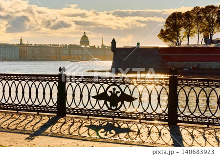 Isaac cathedral, Winter Palace, picturesque metal railings with a double-headed eagle and the crown of the Russian Empire on embankment in St. Petersburg, autumn sunset, incredible sun glare, Russia Isaac cathedral, Winter Palace, picturesque metal railings with a double-headed eagle and the crown of the Russian Empire on embankment in St. Petersburg, autumn sunset, incredible sun glare, Russia 140683923