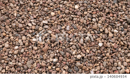 Dense arrangement of small rounded pebbles in mixed beige, brown, gray, and pink tones, forming a natural textured surface with even daylight and no visible horizon or objects 140684934
