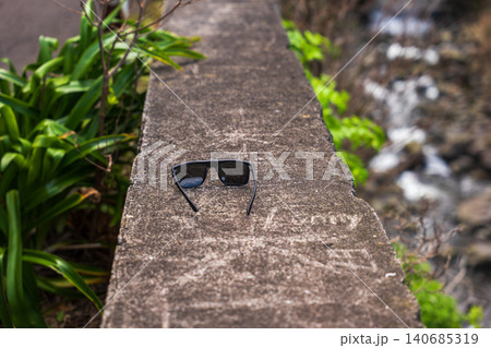 Black sunglasses on weathered ledge by ravine in Madeira miradouro Black sunglasses on weathered ledge by ravine in Madeira miradouro 140685319