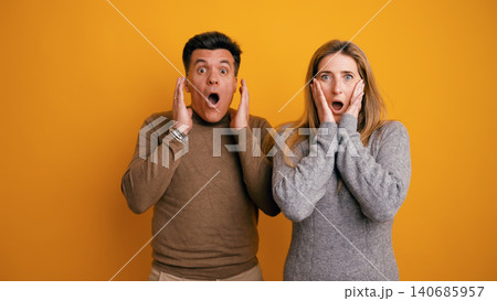 Couple expressing shock and surprise on yellow background Couple expressing shock and surprise on yellow background 140685957