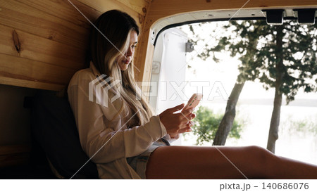Woman relaxing inside camper van using smartphone Woman relaxing inside camper van using smartphone 140686076