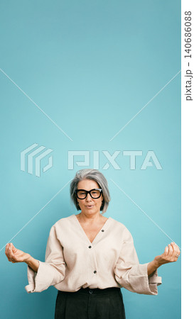Mature woman meditating finding inner peace on blue background Mature woman meditating finding inner peace on blue background 140686088