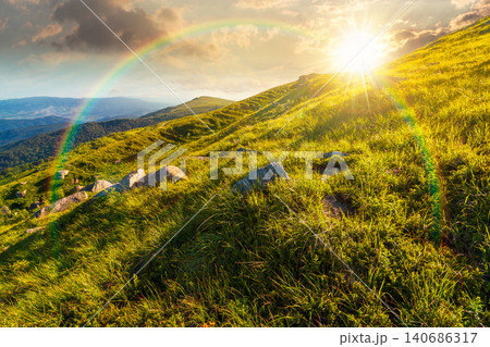 sunset over mountain landscape with grass and rock on a slope. view in to the distant valley of carpathian mountains. mountainous scenery of ukraine in summer. weather with rainbow sunset over mountain landscape with grass and rock on a slope. view in to the distant valley of carpathian mountains. mountainous scenery of ukraine in summer. weather with rainbow 140686317