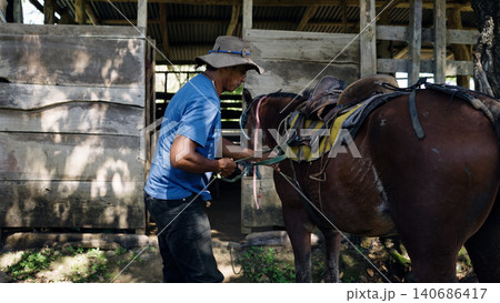 Latino man saddling a horse near a stable Latino man saddling a horse near a stable 140686417