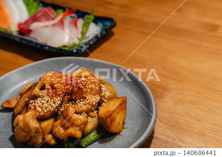 居酒屋風の木製テーブルに並ぶ和食メニューの刺身と鶏肉炒め物 140686441