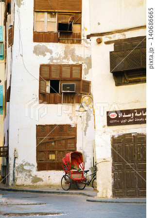 Jeddah, Saudi Arabia- Mar 08 2023, view of the wall of an Arab house with mashrabiya balconies, a red tourist bicycle stroller stands nearby, in the old city of Jeddah, Saudi Arabia 140686665