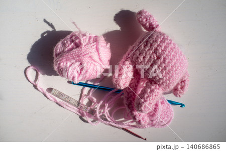 Pink crochet yarn project with hook and handmade fabric pieces on bright white surface Pink crochet yarn project with hook and handmade fabric pieces on bright white surface 140686865