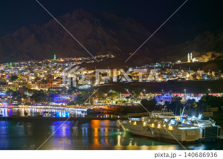 Aqaba, Jordan - Mar 13 2023, an aerial view of night city Aqaba with many of lights, with ship on foreground, at nighttime, Aqaba, Jordan Aqaba, Jordan - Mar 13 2023, an aerial view of night city Aqaba with many of lights, with ship on foreground, at nighttime, Aqaba, Jordan 140686936