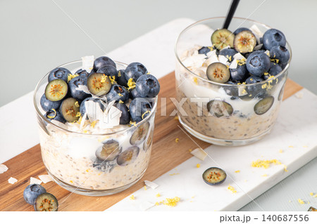 Healthy blueberry Lemon Overnight Oats topped with blueberries, lemon zest and coconut shavings on a light blue wooden counter. Concept for healthy eating and nutrition. Healthy blueberry Lemon Overnight Oats topped with blueberries, lemon zest and coconut shavings on a light blue wooden counter. Concept for healthy eating and nutrition. 140687556