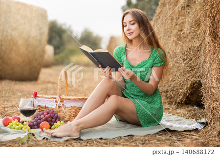 Dreamy young woman wearing in green dress sitting and reading book on soft mat near stack of straw, glamour and fashion photography Dreamy young woman wearing in green dress sitting and reading book on soft mat near stack of straw, glamour and fashion photography 140688172
