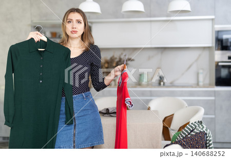 Young upset woman choosing which dress to wear Young upset woman choosing which dress to wear 140688252