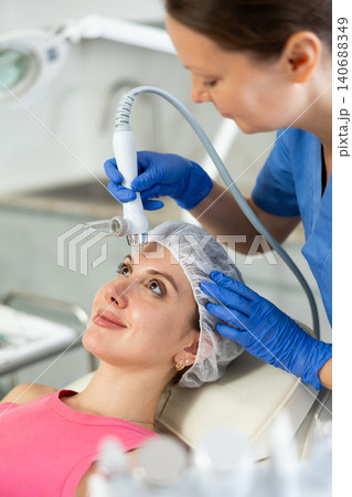 Adult woman cosmetologist doing moisturizing procedure to young woman Adult woman cosmetologist doing moisturizing procedure to young woman 140688349