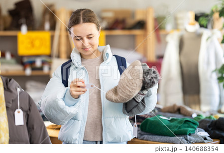 Teenager girl choose hat for autumn-winter season in clothing store Teenager girl choose hat for autumn-winter season in clothing store 140688354