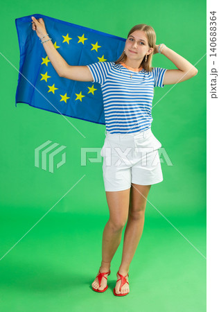 Teenage girl in white shorts with large flag of European Union posing on green background. Chroma key compositing Teenage girl in white shorts with large flag of European Union posing on green background. Chroma key compositing 140688364