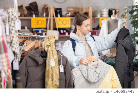 Teen girl choosing down jacket in clothing store Teen girl choosing down jacket in clothing store 140688445