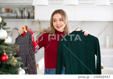 Young smiling woman choosing which dress to wear Young smiling woman choosing which dress to wear 140688447